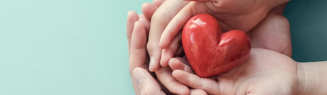 A mother, father, and child's hands holding a porcelain heart